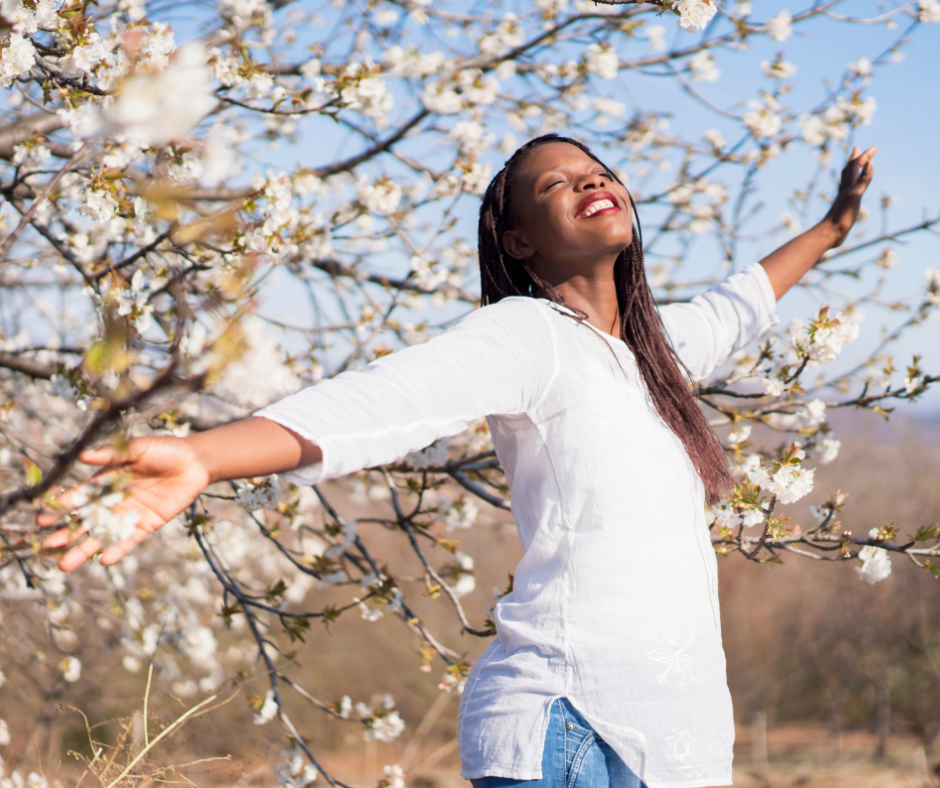 Photo of joyful woman with open arms beside a cherry blossom.